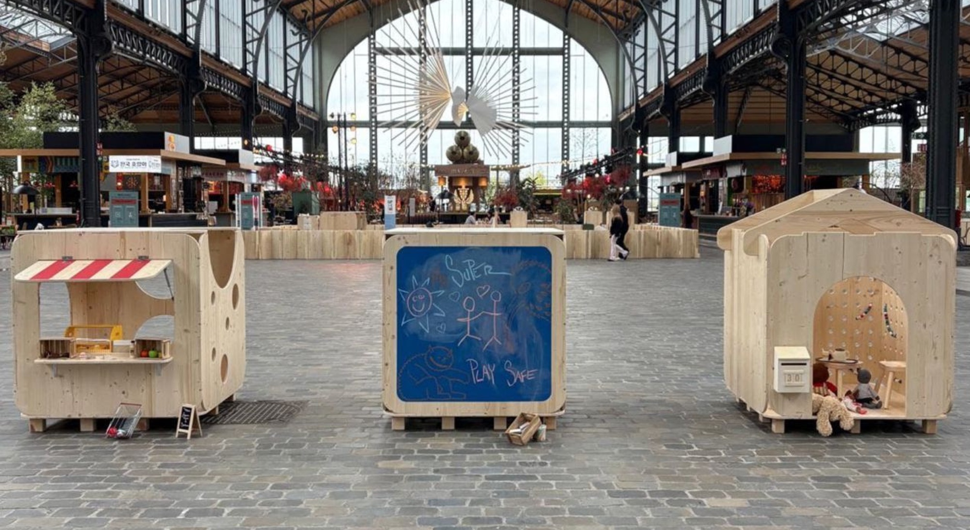 Trois boxes en bois dans la halle : une échoppe à auvent rayé, un tableau noir dessiné, une maisonnette